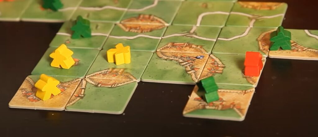 colorful meeple stand on the Carcassonne classic map tiles